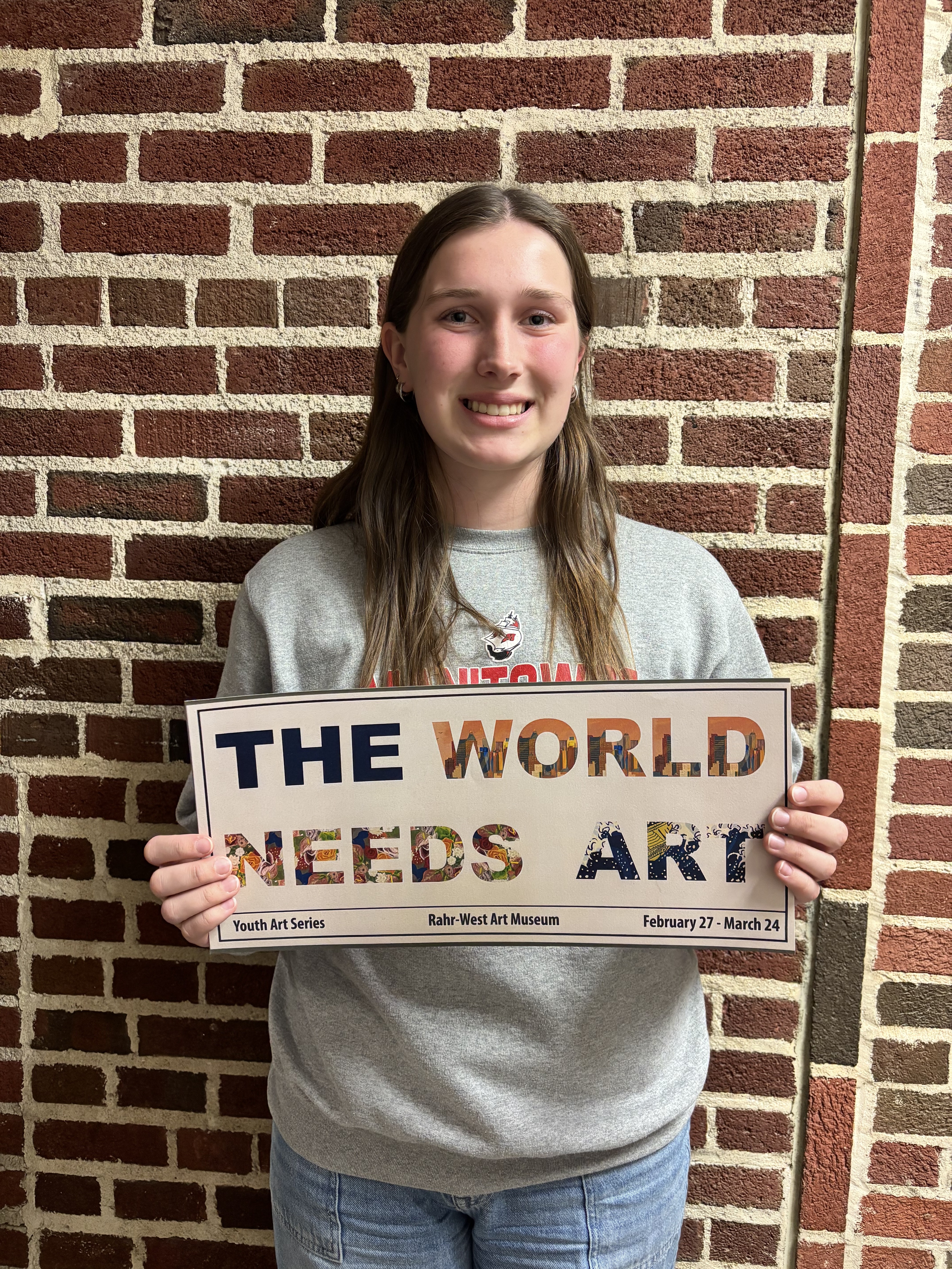 JULIA TUMA HOLDING HER BILLBOARD MOCK UP "THE WORLD NEEDS ART" 