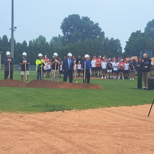 district leaders and project managers breaking ground on new field with students in the background