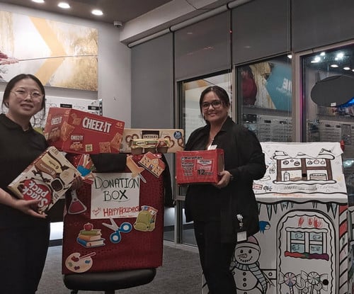 TWO EYEMART EMPLOYEES STANDING NEXT TO DONATION THEY COLLECTED FROM THE COMMUNITY