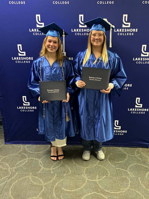 Elizabeth Leikam and Aubrey White standing in cap in gown with their certificates