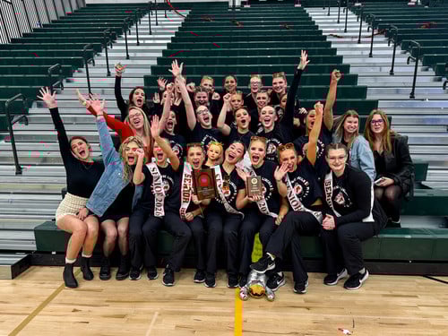 dance team sitting on bleachers cheering with their trophy