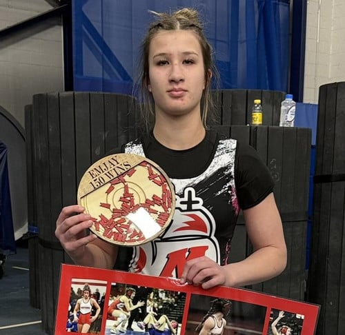 Emjay Nuemann holding a poster filled with pictures of her wrestling and a wood plaque that says  