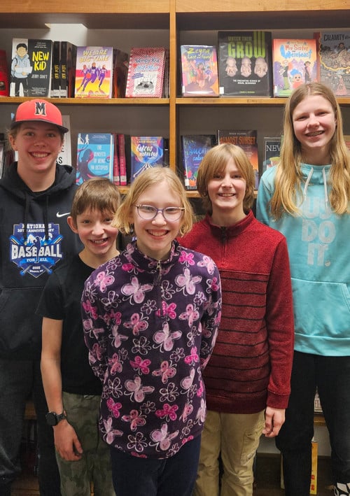students standing smiling in front of a book case filled with books