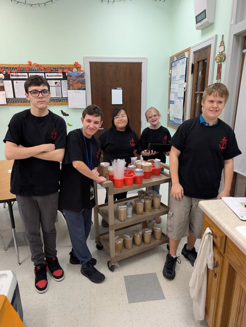 5 students stand by a coffee cart in black shirts with a red anchor that says Shipyard Coffee
