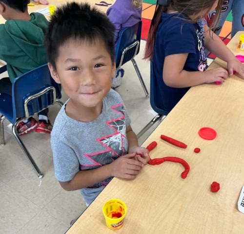 student sits at table with red play dough that spells out 