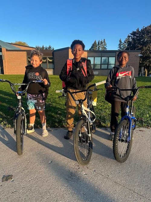 3 students stand with their bikes outside of the school