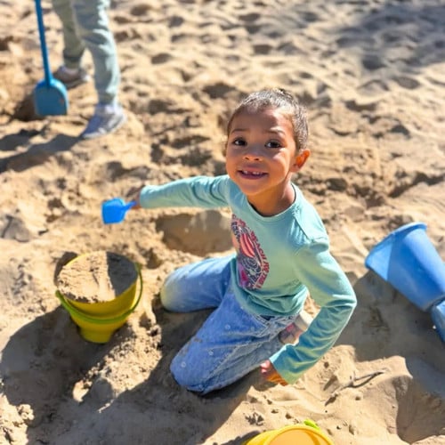 student shovels sand into a bucket on the beach