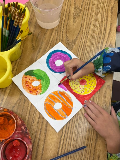 students hands painting 4 colorful donuts drawn on white paper