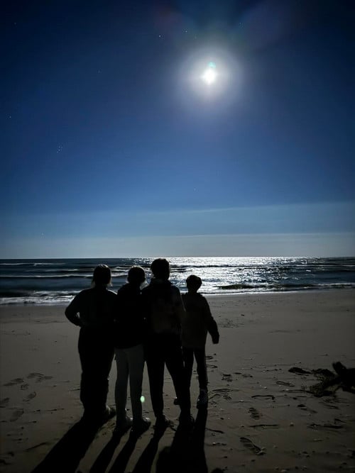 Students stand on beach looking at moon